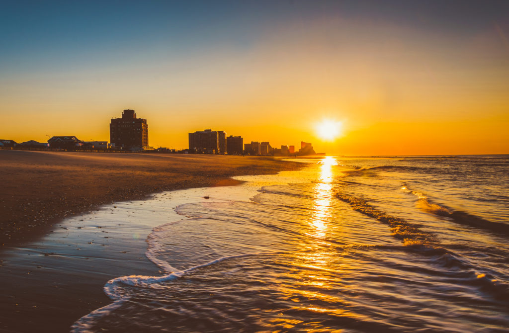 Golden sunrise over ocean waves with coastal city skyline silhouette