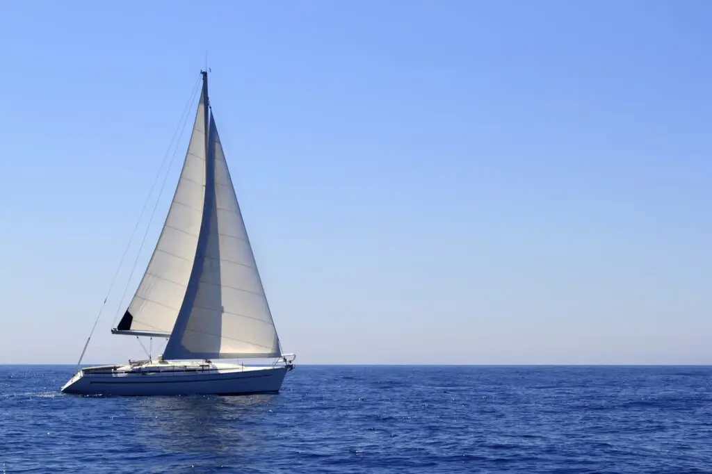 White sailboat with full sails gliding across calm blue open water under a clear sky.