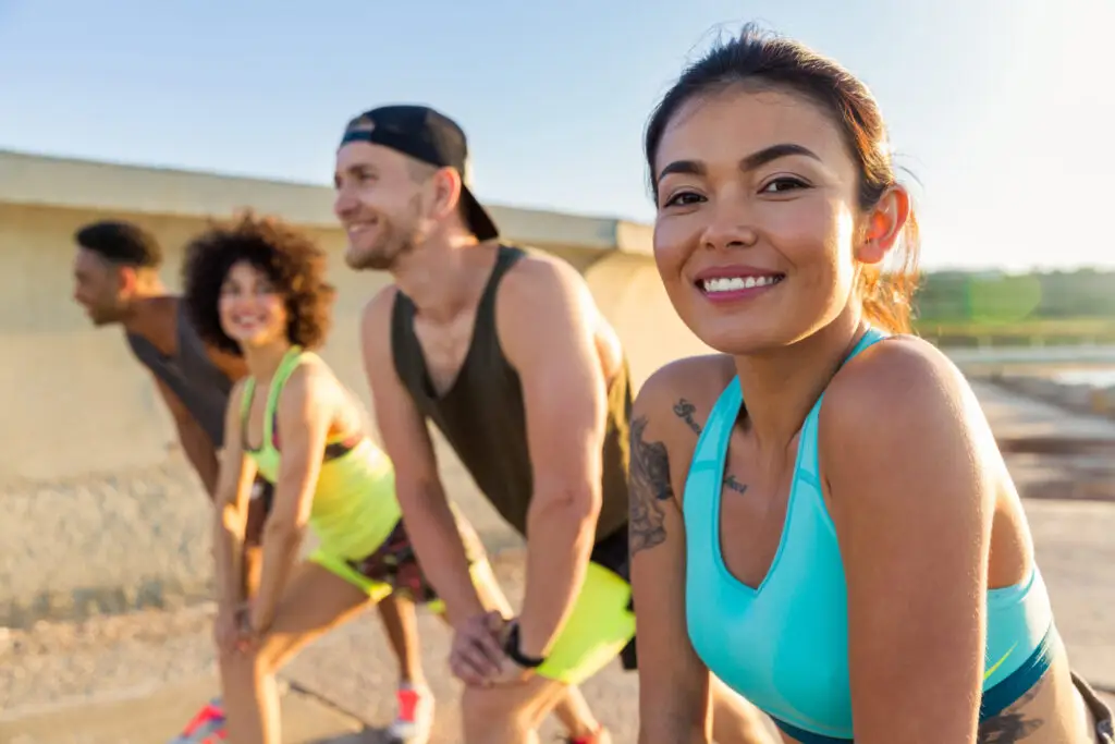 Smiling diverse group of friends stretching outdoors in athletic wear during a sunny workout session.
