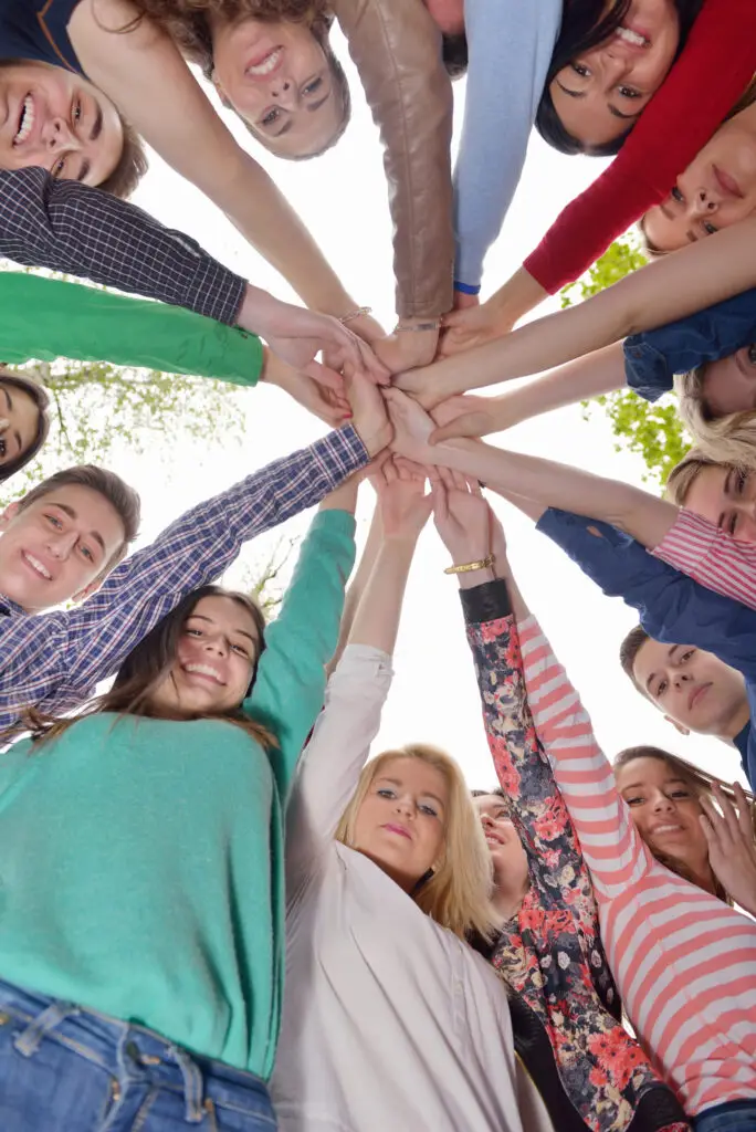 Group of smiling people standing in a circle joining hands together in unity, viewed from below.